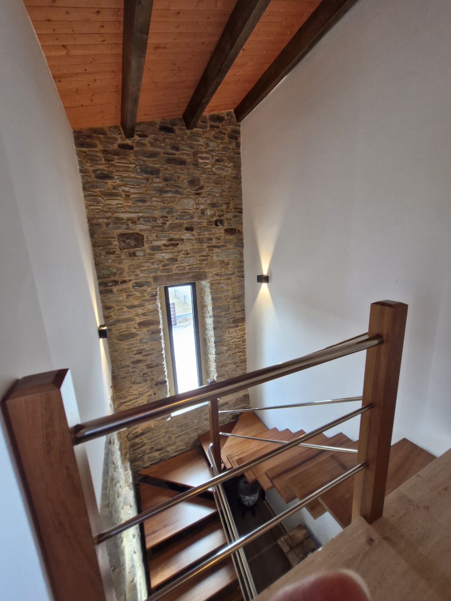 Escalera flotante de madera con muro de piedra iluminado